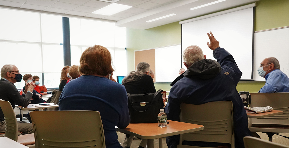 Image of class from the back with one person raising their hand