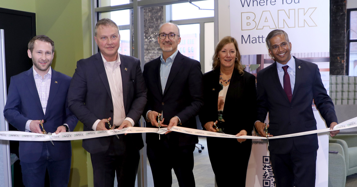Five people smiling, ready to cut ribbon at event